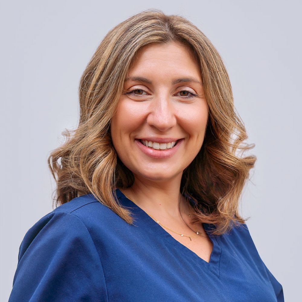 Portrait of a smiling woman in a blue top with curly blonde hair.
