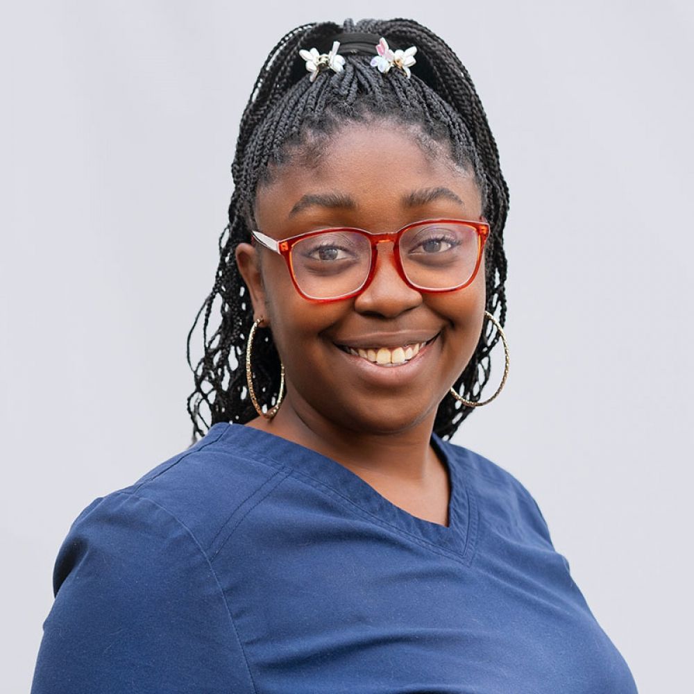 Young woman with braided hair and red glasses smiling at the camera.