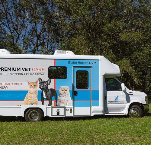 Mobile veterinary hospital vehicle parked on grass with images of pets on its side.